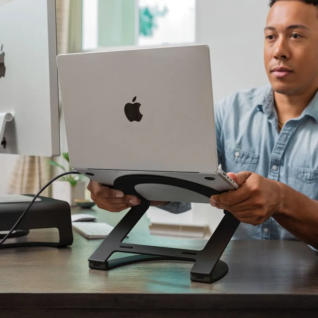 Användaren justerar MacBook på vitt Twelve South Curve Flex-stativ för ergonomisk inställning av arbetsytan