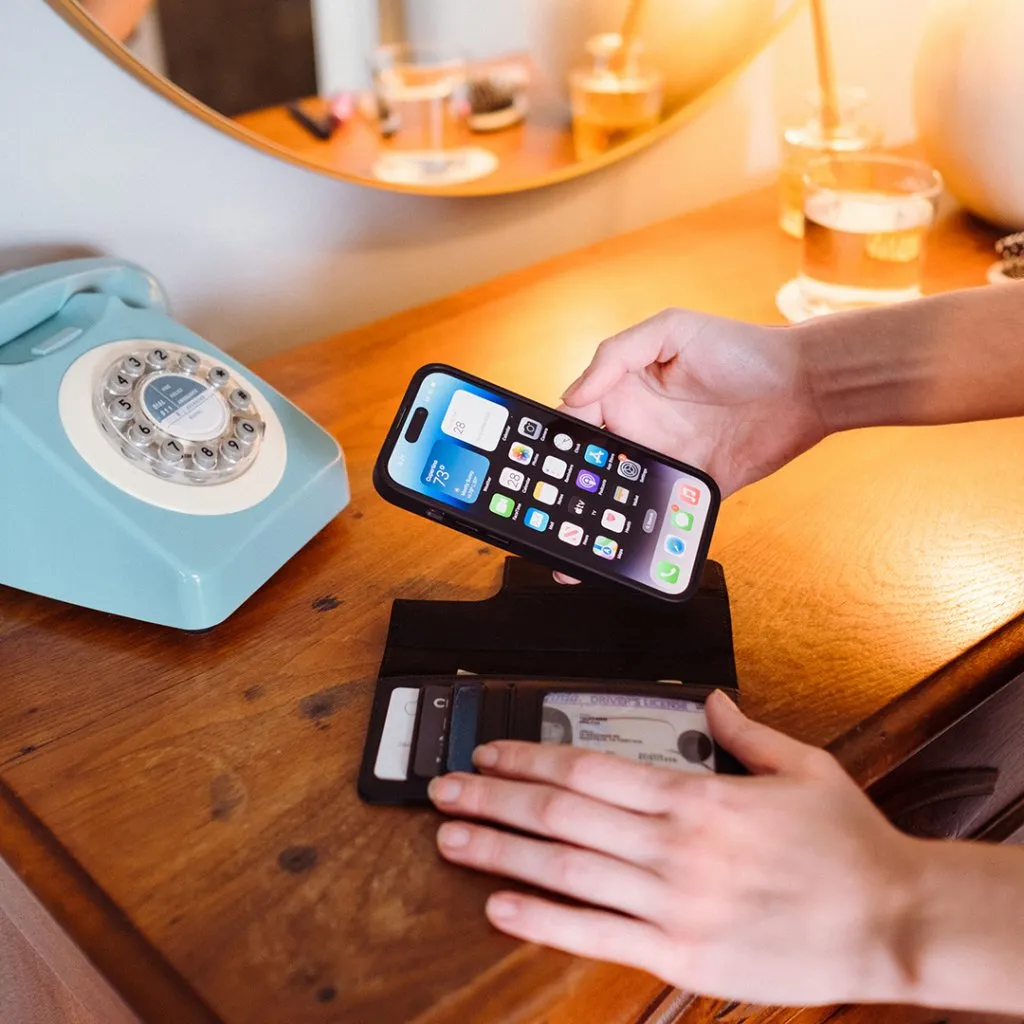 Användaren håller i en svart Twelve South BookBook med MagSafe för iPhone 14 Pro, som visar plånboksfunktionen och den förstklassiga läderdesignen.