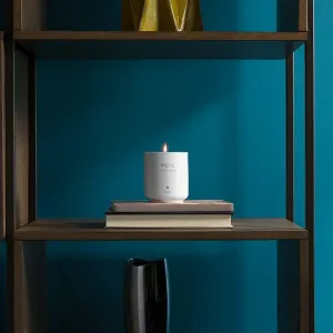 Twelve South Inspire Mac Candle No. 2, et tent hvitt duftlys i en merket beholder på stablede bøker.