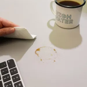 Twelve South DeskPad vegannahast lauamatt toonis Dove Grey, mida näidatakse pärast kohvi mahaloksumist puhtaks pühitavana