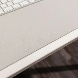 Twelve South deskPad helehall tekstuuriga lauamatt reljeefse logoga, näidatud valge klaviatuuri kõrval