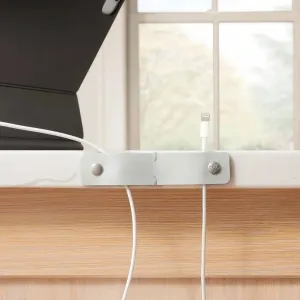 Twelve South CableSnap Stay grå kabelholder i læder, der holder et hvidt opladningskabel på kanten af et skrivebord