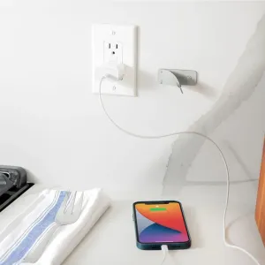 Twelve South CableSnap Stay-kabelholder monteret ved siden af en stikkontakt, der fører et opladningskabel til en telefon.