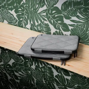 Twelve South SuitCase gråt quiltet MacBook-etui med hård skal og lynlås, vist stablet på en træhylde.