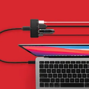 Twelve South StayGo mini USB-C šakotuvas, prijungtas prie nešiojamojo kompiuterio keliais kabeliais, raudoname fone.