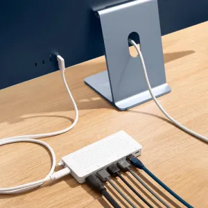 Twelve South StayGo USB-C-hub i hvitt med tilkoblede kabler på et skrivebord ved siden av et skjermstativ.