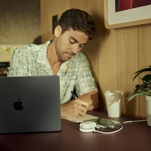 Twelve South ButterFly SE 2-in-1 Qi2 įkroviklis ant stalo, įkraunantis iPhone ir AirPods šalia užrašinės.