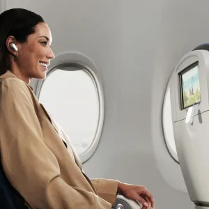 Twelve South AirFly langaton äänilähetin kytkettynä lentokoneen istuimen selkänojan näyttöön matkustajan vieressä, jolla on nappikuulokkeet.