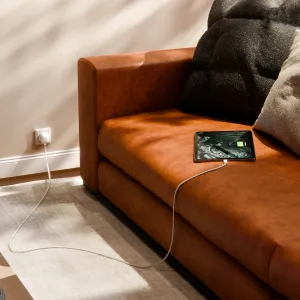 Twelve South USB-C-laturi integroidulla EU-pistokkeella lataamassa tablettia ruskean nahkasohvan vieressä.