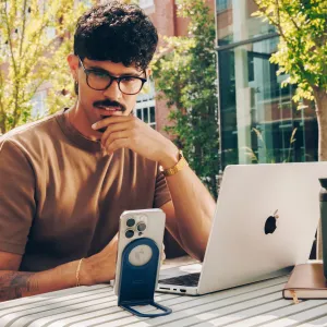Twelve South Curve Nano blått hopfällbart telefonställ som håller en smarttelefon upprätt bredvid en bärbar dator utomhus