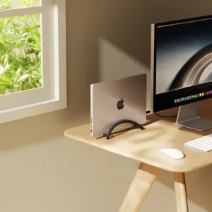 Twelve South BookArc Flex vertical laptop stand holding a MacBook beside a monitor on a wood desk