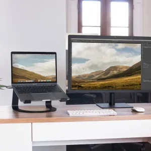 Support pour ordinateur portable Twelve South Curve en noir mat, avec un ordinateur portable installé à côté d’un moniteur externe sur un bureau.