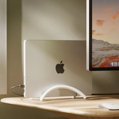 Hvitt, buet vertikalt stativ som holder en bærbar datamaskin oppreist på skrivebordet; venstre side med synlige porter og tilkoblet kabel.