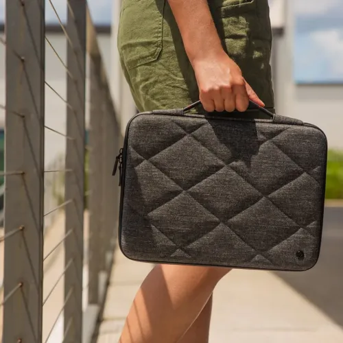 Mørkegrå vattert laptopveske med innfelt håndtak og avrundede hjørner, glidelås langs kanten og liten logo i nederste hjørne