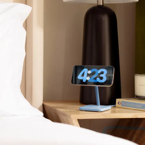 Twelve South HiRise 2 Deluxe in glacier blue, a slim phone stand with square base and tilted arm, on a bedside table.