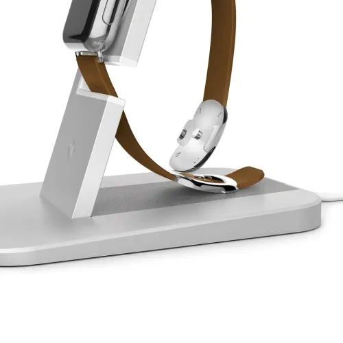 Sidabro spalvos "Apple Watch" laikrodžio stovas su kampiniu laikikliu ir oda dengtu pagrindu, laikrodis su pritvirtintu rudu dirželiu, gale - baltas laidas.