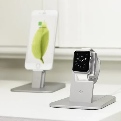 Sidabrinės spalvos "HiRise" laikrodžio "Apple Watch" stovas, L formos laikiklis ant stačiakampio formos pagrindo, laikrodis pritvirtintas priekyje, padėtas ant balto paviršiaus.