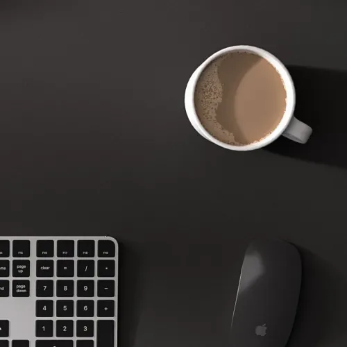 Sort DeskPad med let struktureret overflade, med hvidt kaffekrus på toppen, sort mus til højre og hjørne af numerisk tastatur.