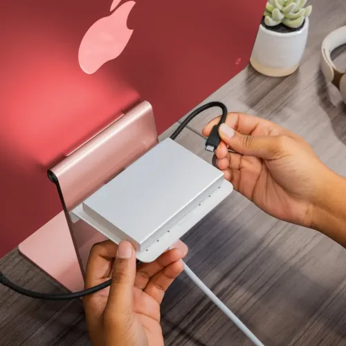 BackPack 4 alumīnija plaukts, kas uzstādīts uz iMac statīva aizmugures, ar nelielu ierīci virsū un ar roku savienojamu USB-C kabeli.