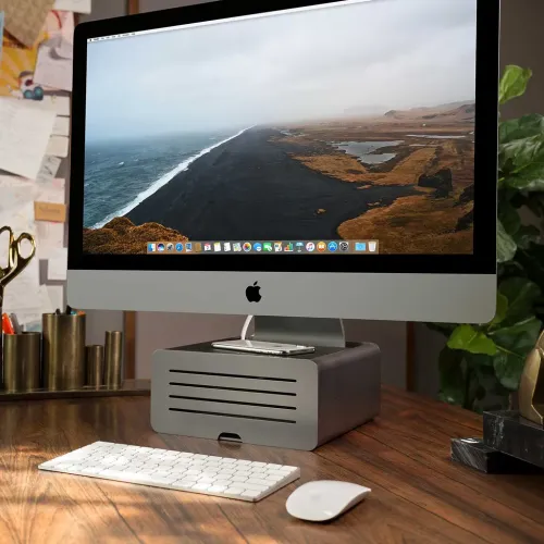 Twelve South HiRise Pro iMac-stativ som höjer en iMac ovanför ett skrivbord, med en telefon vilande ovanpå.