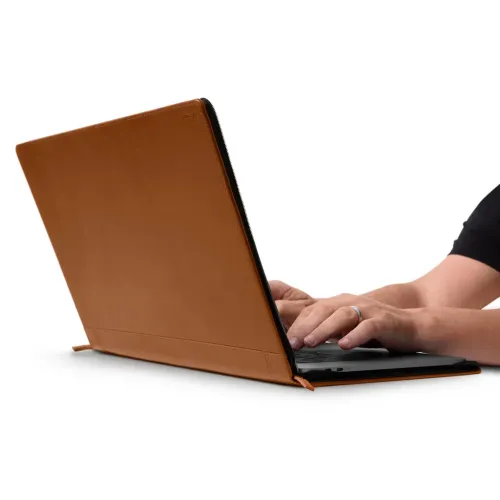 Konjakivärvi nahast ümbris 15-tollisele MacBook Pro-le, mis on avatud fooliumina arvuti ümber ja millel on nähtavad USB-C pordid ja käekiri.