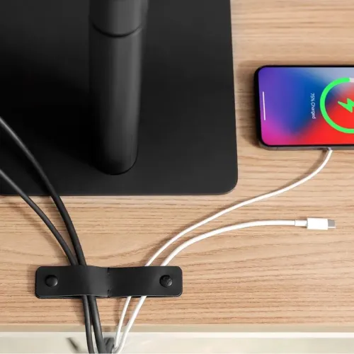 CableSnap Stay kabelholder i lær med to trykknapper festet til skrivebordet, holder kablene nær kanten ved siden av en smarttelefon.