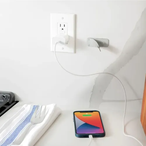 Twelve South CableSnap Stay-kabelhållare monterad bredvid ett vägguttag, där den leder en laddningskabel till en telefon.