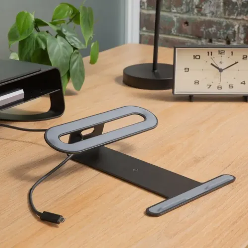 MacBook- og iPad-stativ i matt svart metall, vinklet med ovalt kabelhull, gummiputer og slank skrivebordsprofil.