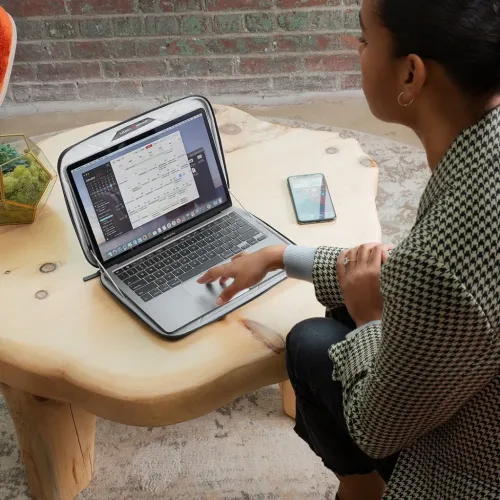 Twelve South SuitCase MacBookin kanssa harmaassa kovakuorisessa kotelossa, jossa on kaksinkertaiset vetoketjut ja upotettu kahva, täysin auki työtä varten.