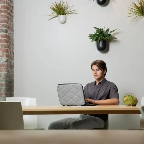 Harmaa tikattu MacBookin kotelo, jossa on timanttikuvio; avoin tietokoneen ympärillä pöydällä, musta vetoketju koko reunalla.