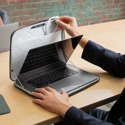 MacBook-kotelo, jossa on tikattu sisustus, joustavat kulmahihnat ja tasku kannessa; tietokonetta käytetään kotelossa, kaapeli on irrotettu.