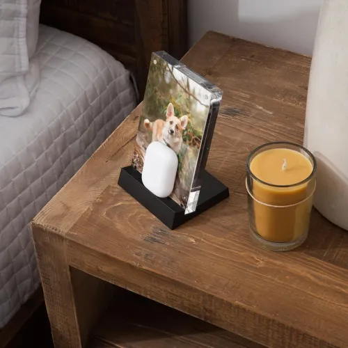 PowerPic Mod trådløs laderamme med gjennomsiktig fotoramme og hvitt hodetelefonetui på svart sokkel, på et nattbord av tre.