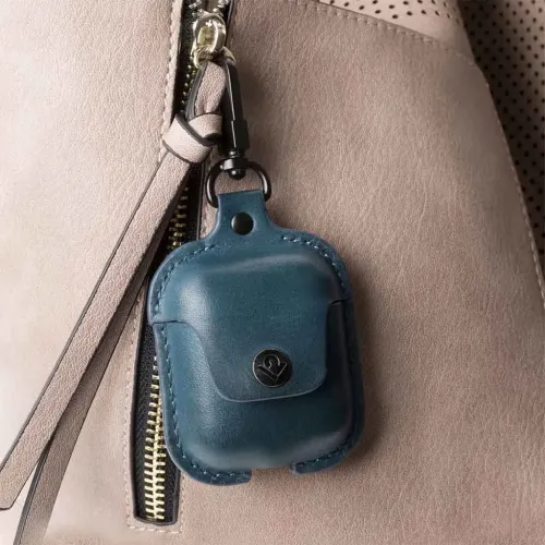 Sininen AirPods-nahkakotelo, jossa on kansi ja painike, kiinnitetty mustalla karabiinilla vaaleaan laukkuun näkyvällä vetoketjulla.