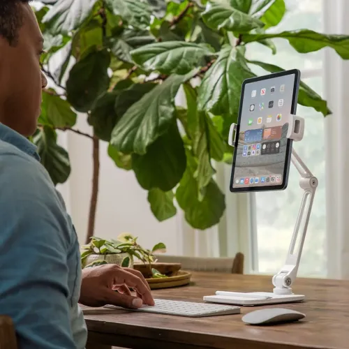 Twelve South HoverBar Duo, valge liigendkäepidemega iPadide statiiv, mis hoiab iPadi laua peal aluse peal klaviatuuri ja hiire kõrval.