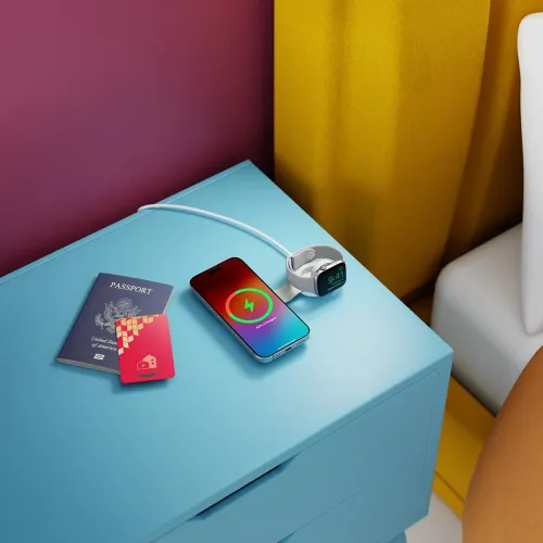 Baltas sulankstomas "2-in-1" įkroviklis "ButterFly SE" su iškiliu laikrodžio laikikliu ir "iPhone" paviršiumi, prijungtas USB-C kabeliu ant mėlyno naktinio stalelio.