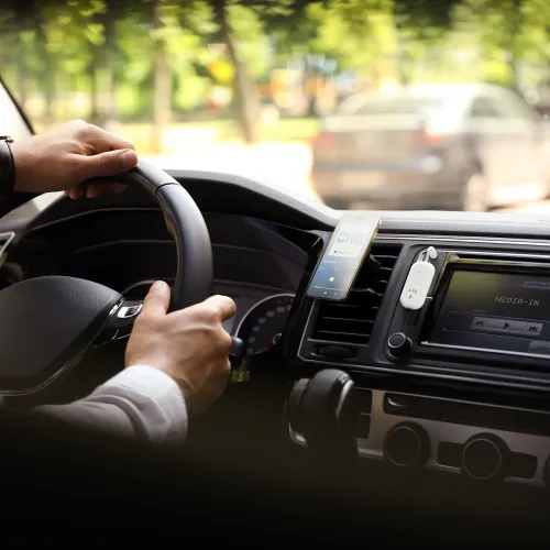 AirFly Pro 2 vit oval ljudadapter med knapp, LED och 3,5 mm-kontakt, fäst vid bilens luftgaller intill stereons skärm fram.