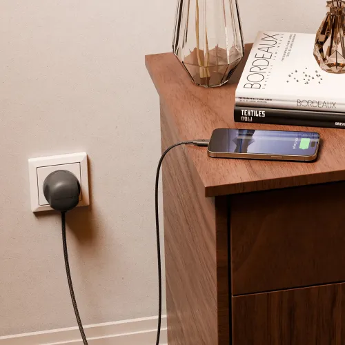 Skifer skjøteledning med rund plugg sitter i EU-stikkontakten, og en flettet kabel går opp til en telefon på et trebord.