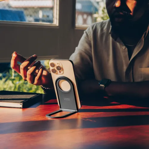Curve Nano-stativ i skiffer, vikbart med ringformad magnetyta och gångjärnsbas, håller en telefon i porträttläge på ett bord