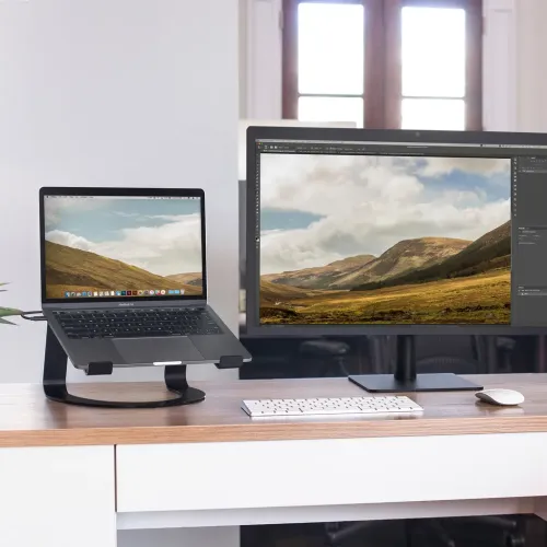 Support pour ordinateur portable Twelve South Curve en noir mat, avec un ordinateur portable installé à côté d’un moniteur externe sur un bureau.
